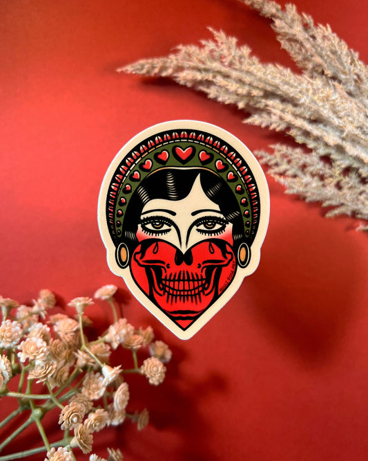 Sticker of a stylized face with skull design on a red background with floral elements.