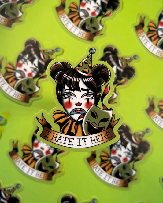 Sticker with a clown face and text 'I HATE IT HERE' on a green background