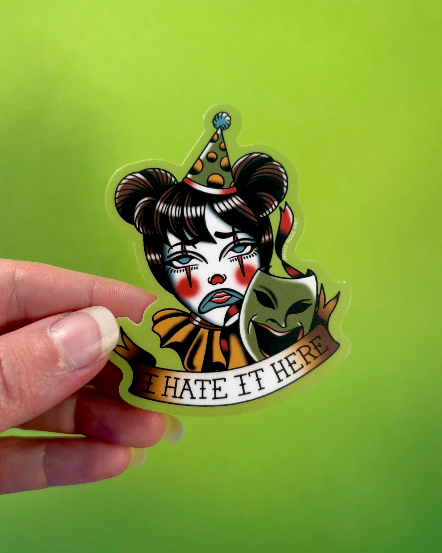 Sticker with a clown face and text 'I HATE IT HERE' on a green background