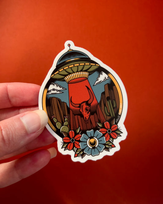 desert scene with a UFO sucking up a bison skull and flowers on the bottom on a sticker