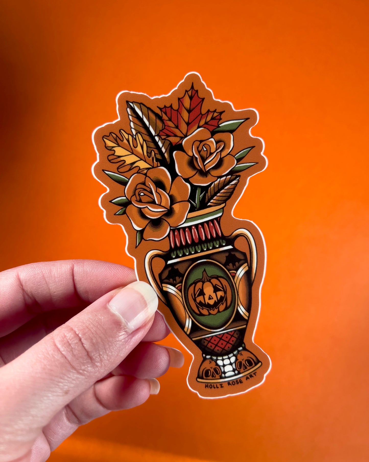 Decorative sticker with floral and vase design held by a hand against an orange background