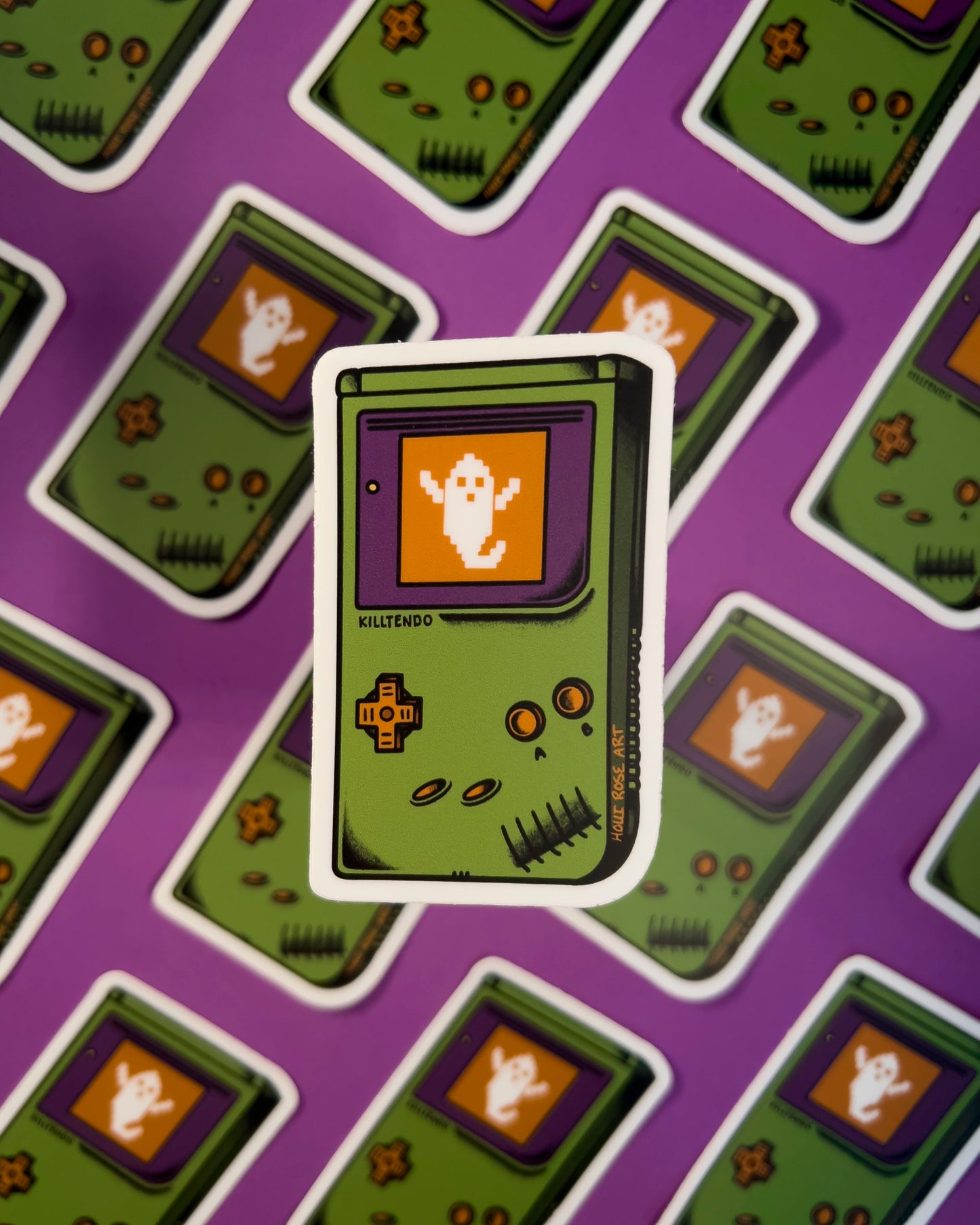 Sticker of a green hand gaming system with a ghost on the screen on a purple background