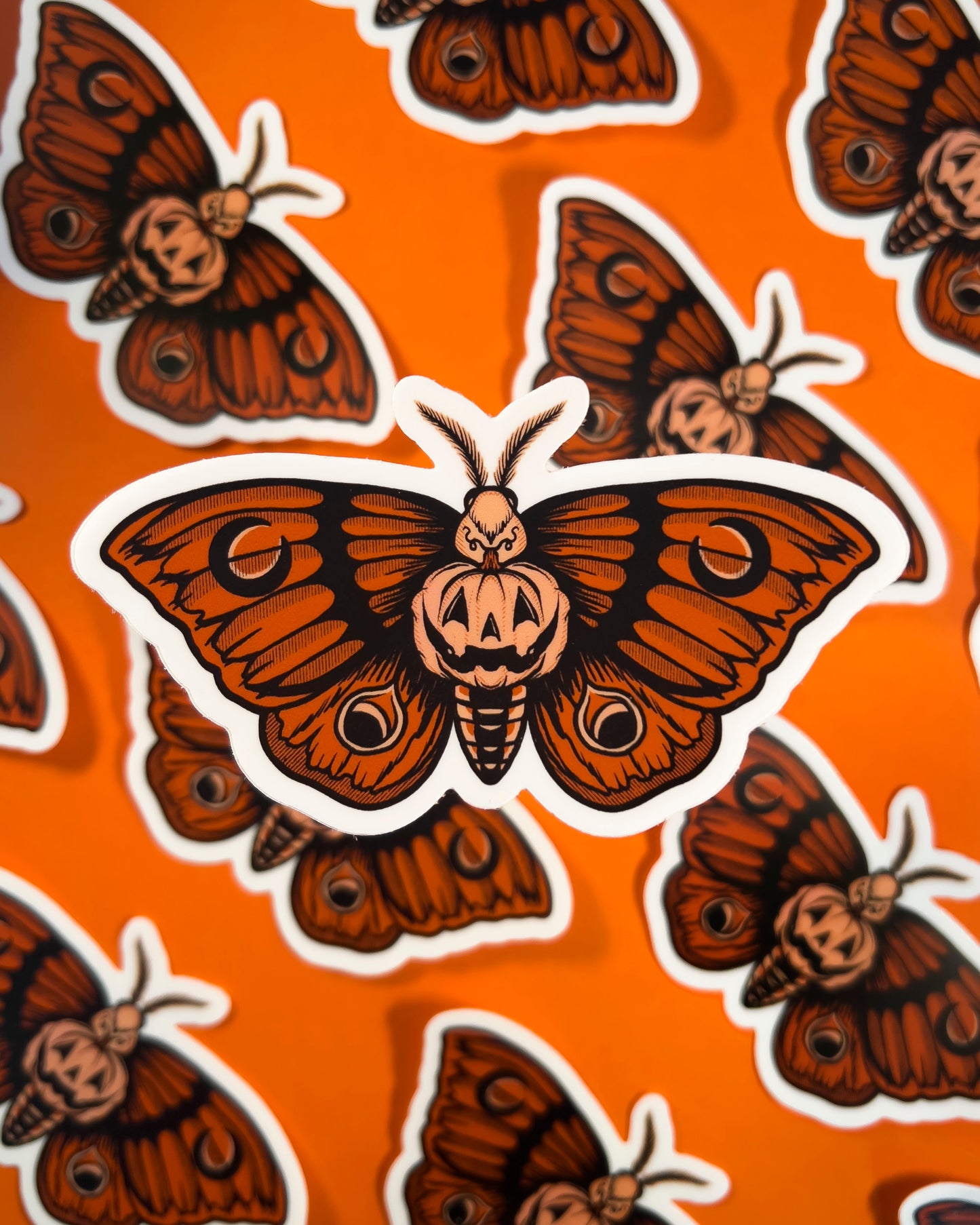 sticker of an orange moth with a pumpkin in the center