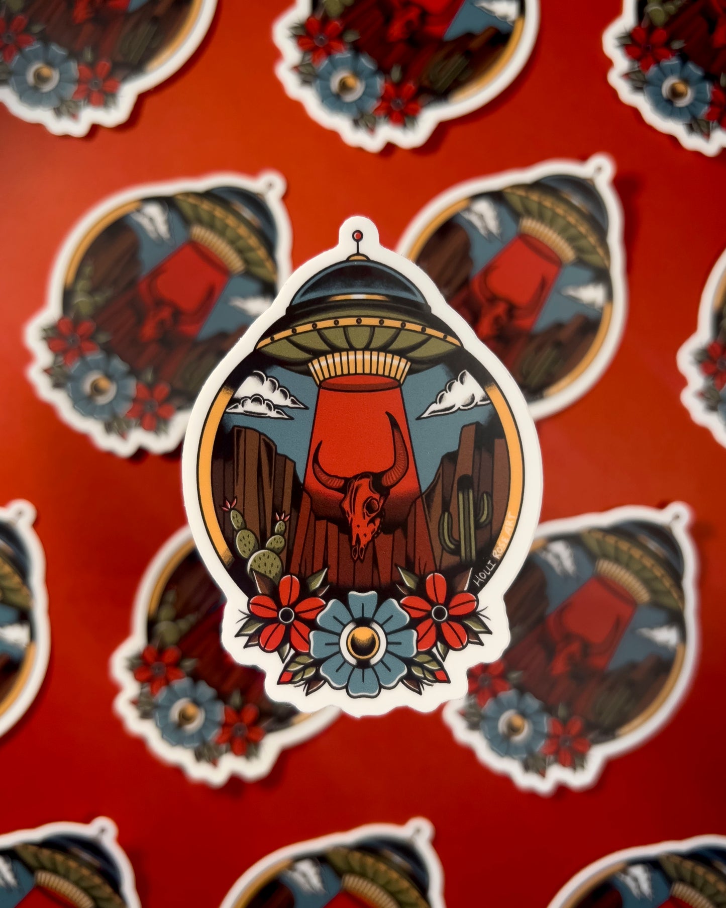 desert scene with a UFO sucking up a bison skull and flowers on the bottom on a sticker