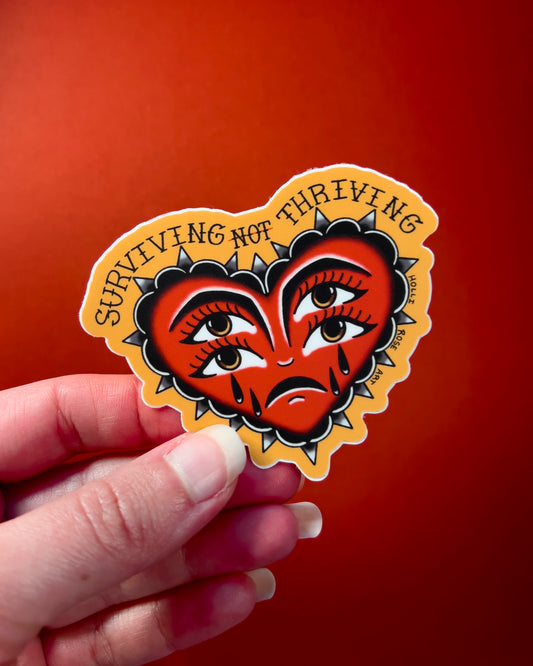 heart sticker with eyes that says "surviving not thriving"
