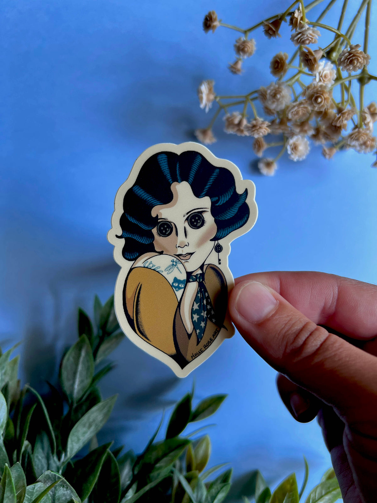 A sticker with a pinup style gal with blue hair, button eyes and a yellow shirt