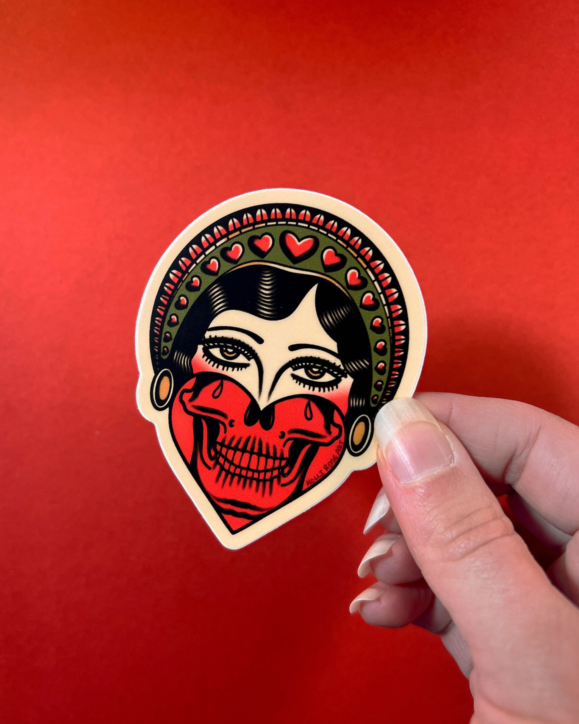 Sticker with a stylized face design held against a red background