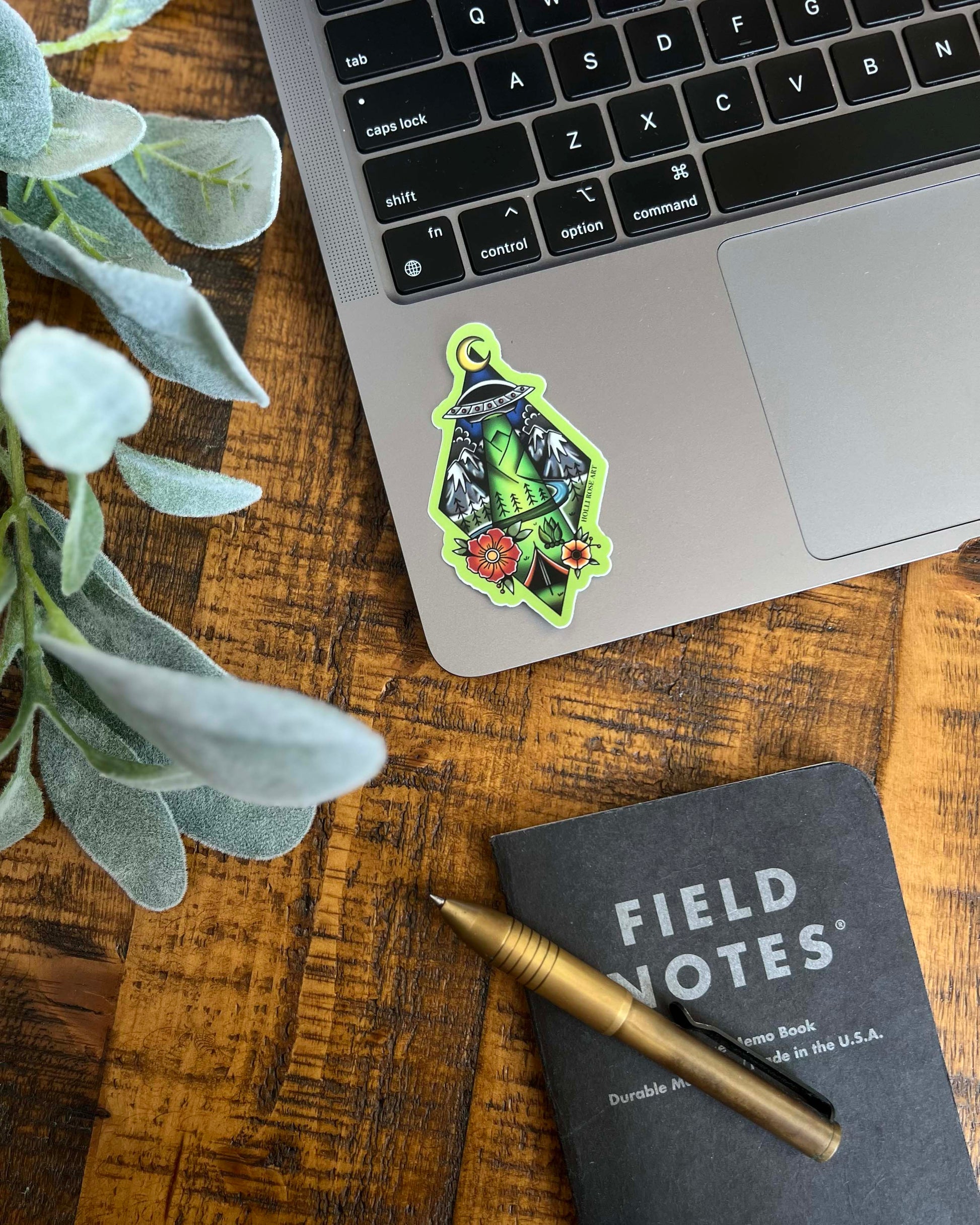 Decorative sticker with nature-themed alien abduction on a laptop