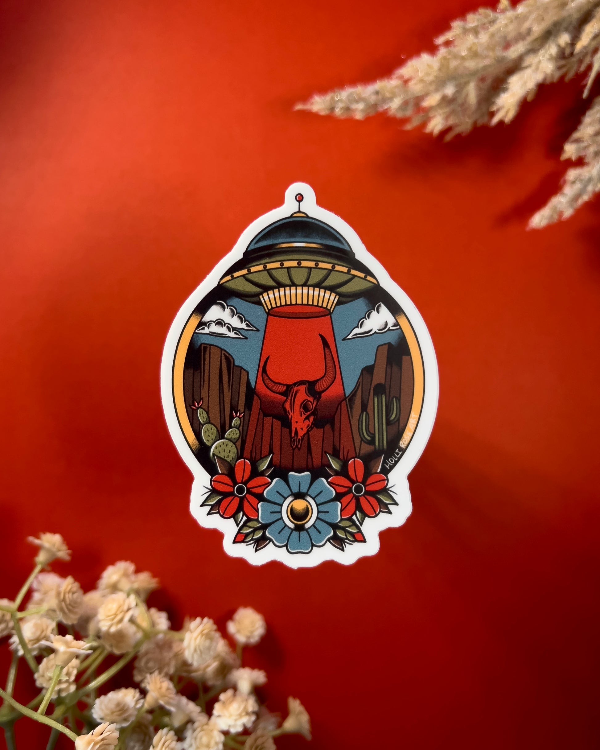 desert scene with a UFO sucking up a bison skull and flowers on the bottom on a sticker