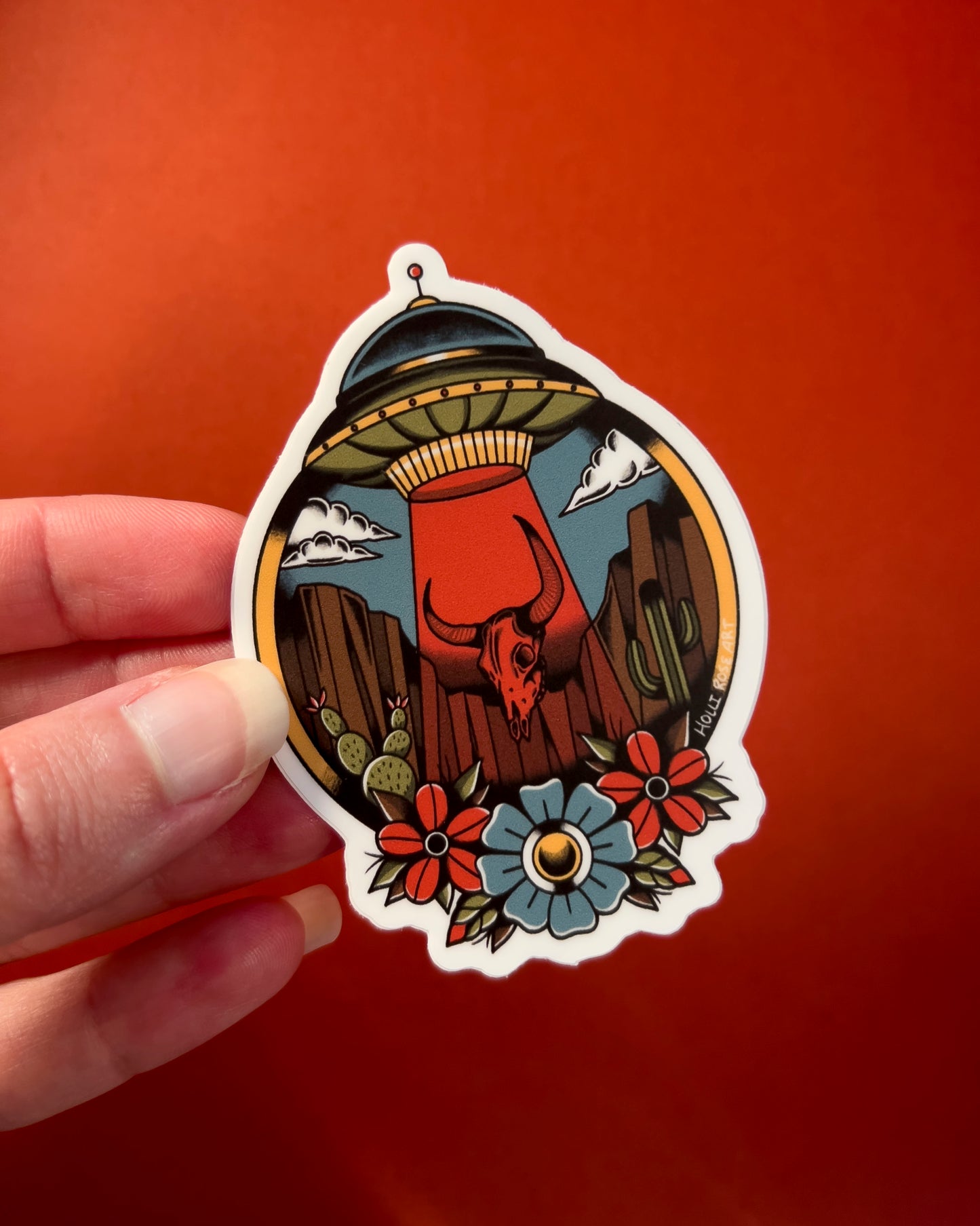desert scene with a UFO sucking up a bison skull and flowers on the bottom on a sticker