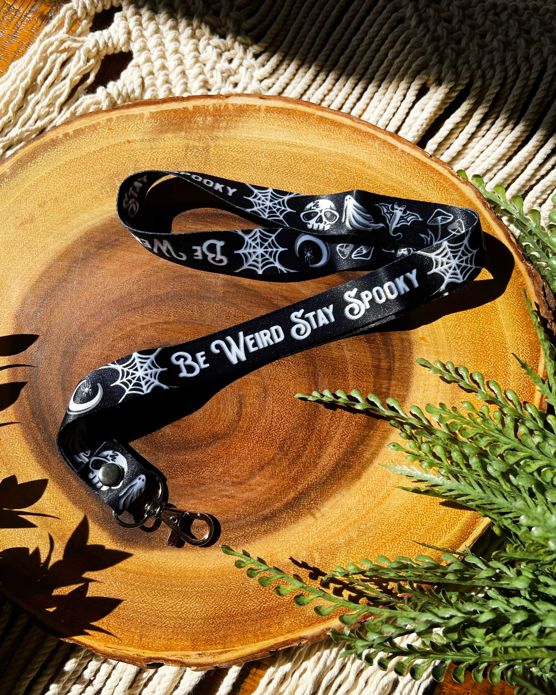 a black lanyard with the words be weird stay spooky and white illustrations