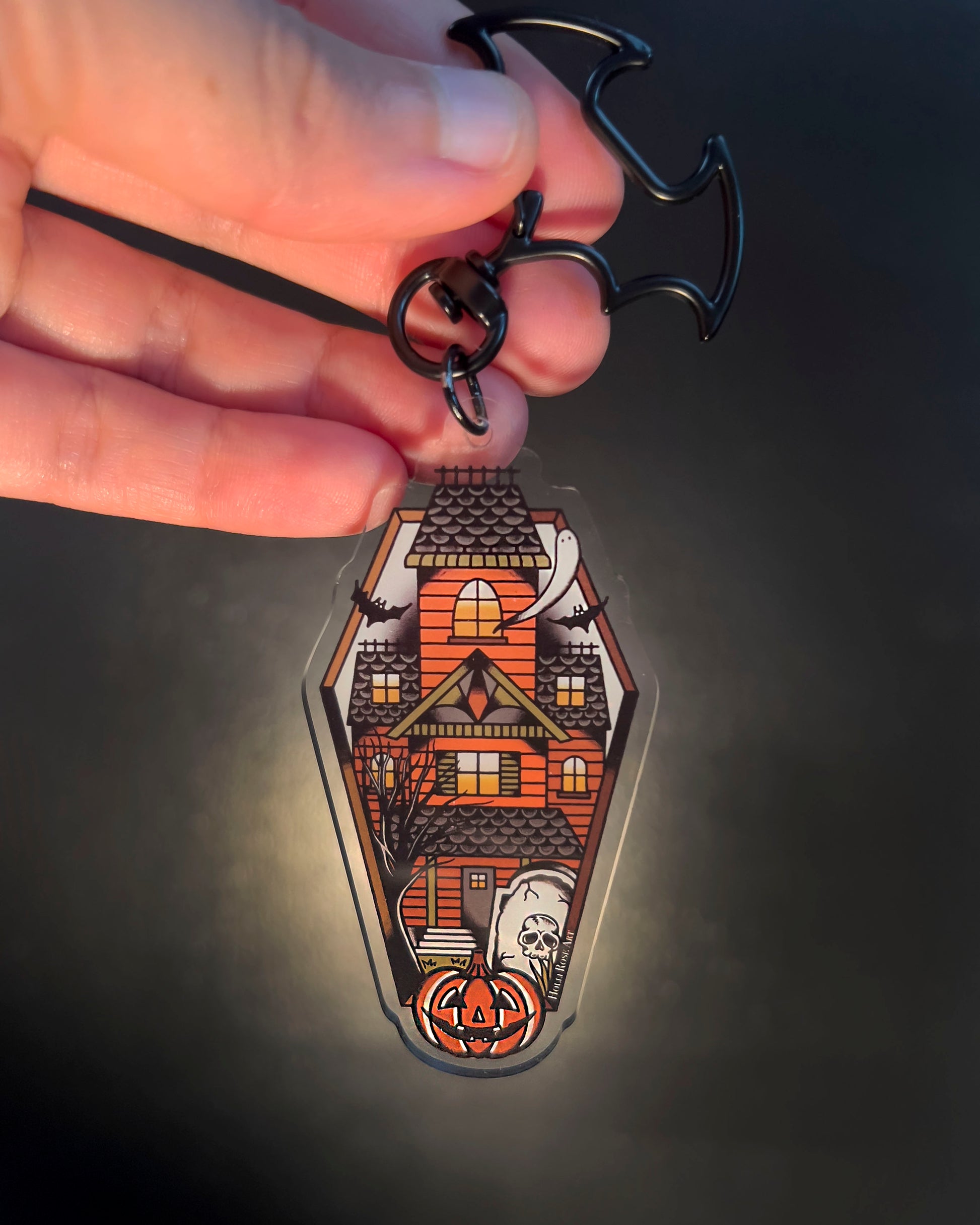 Halloween-themed keychain with a haunted house design held by a hand against a dark background.
