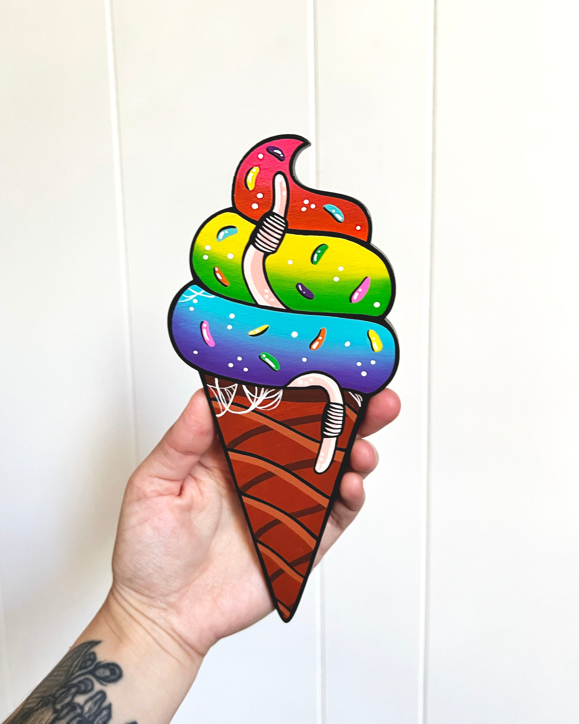Colorful painted ice cream cone held by a hand against a white background