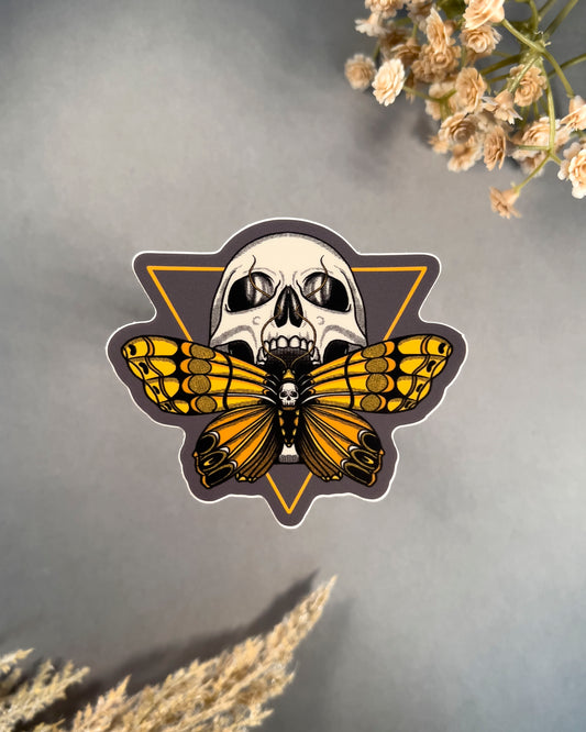 Sticker with a skull and butterfly design on a gray background with flowers.