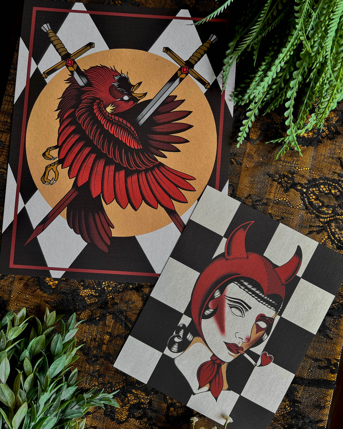 2 art prints - a larger one with a cardinal and two swords going through it and a smaller one with a girl wearing a devil horn headdress and smoking