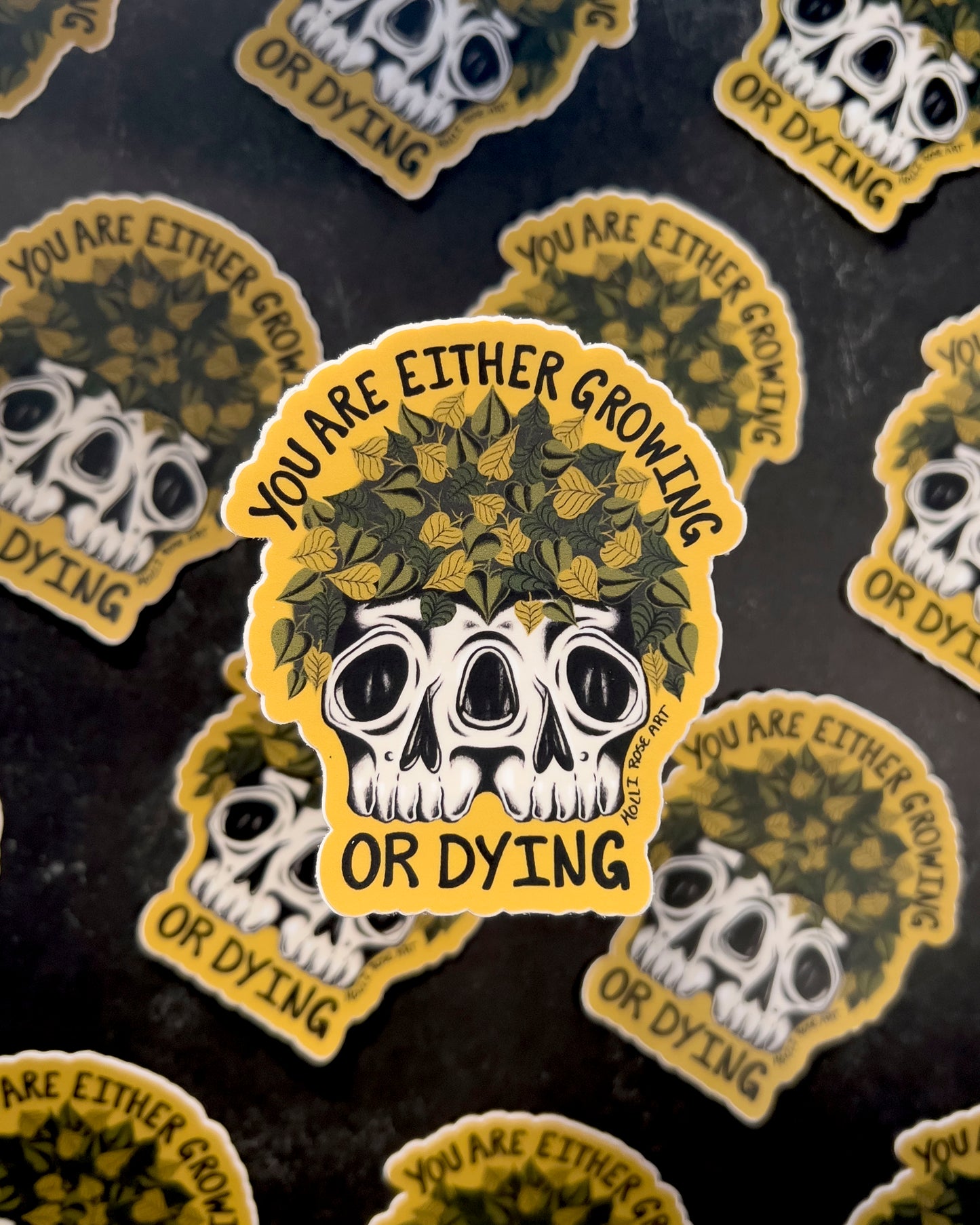 a sticker that says you are either growing or dying with a double headed skull with plants inside