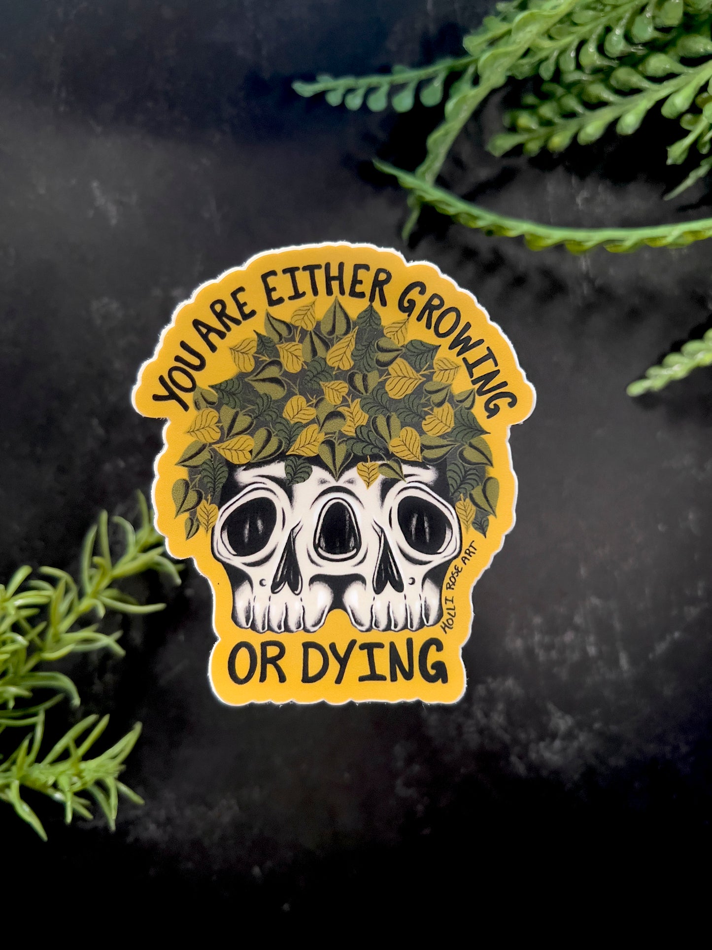 a sticker that says you are either growing or dying with a double headed skull with plants inside