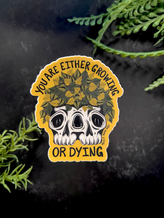 a sticker that says you are either growing or dying with a double headed skull with plants inside