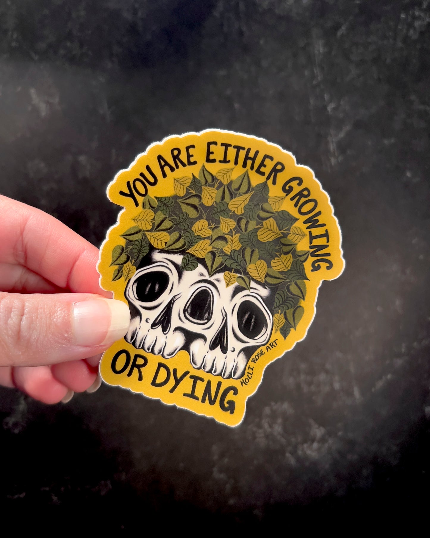 a sticker that says you are either growing or dying with a double headed skull with plants inside