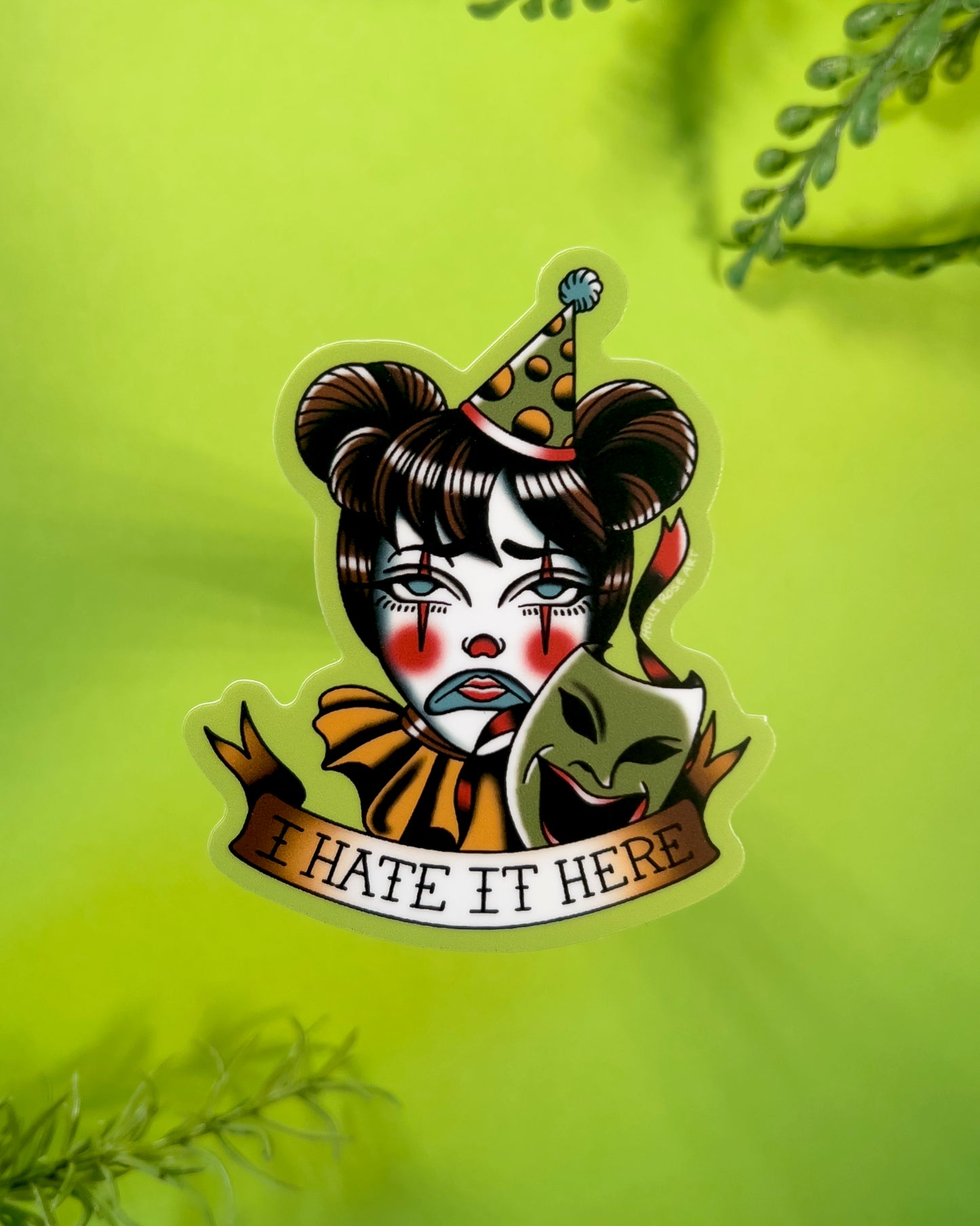 Sticker with a clown face and text 'I HATE IT HERE' on a green background