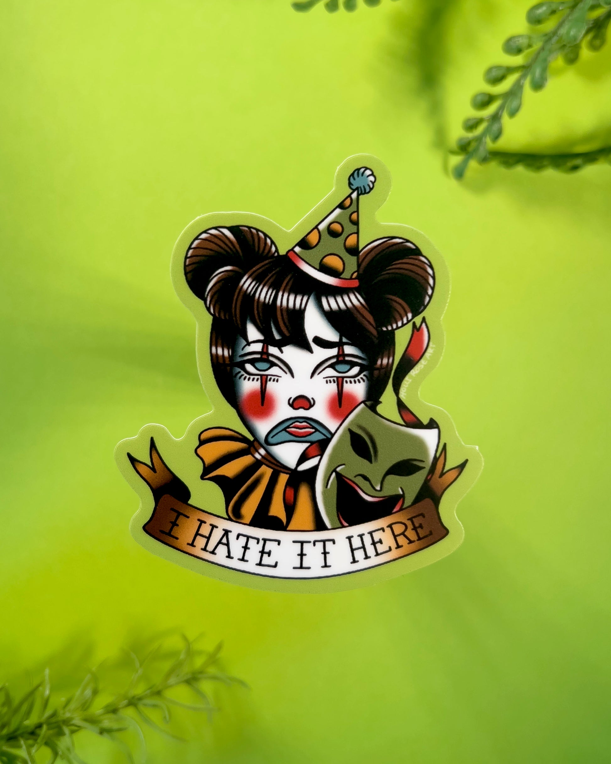 Sticker with a clown face and text 'I HATE IT HERE' on a green background