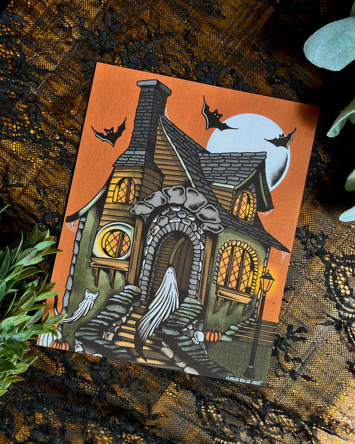 An art print with a ghost and a cat ghost in a cottage with an orange sky and a moon and bats.