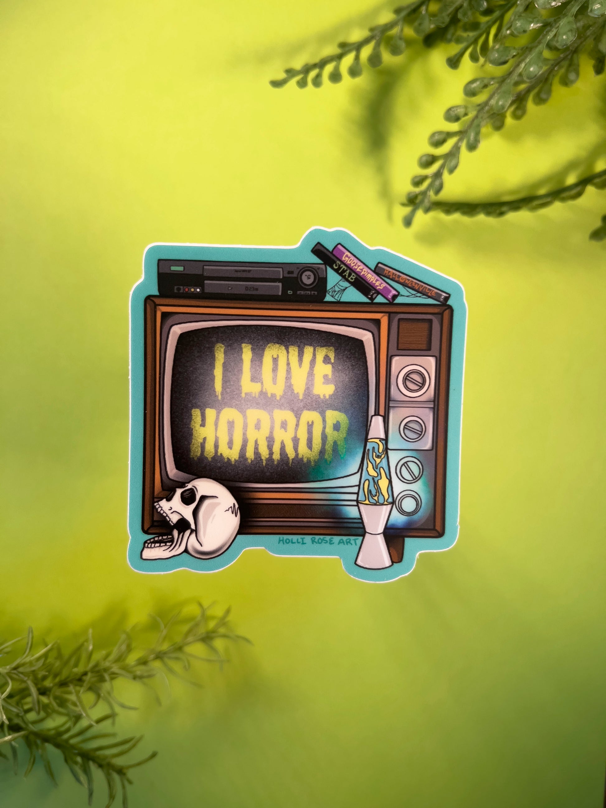 Sticker of a retro TV with 'I Love Horror' text held against a green background