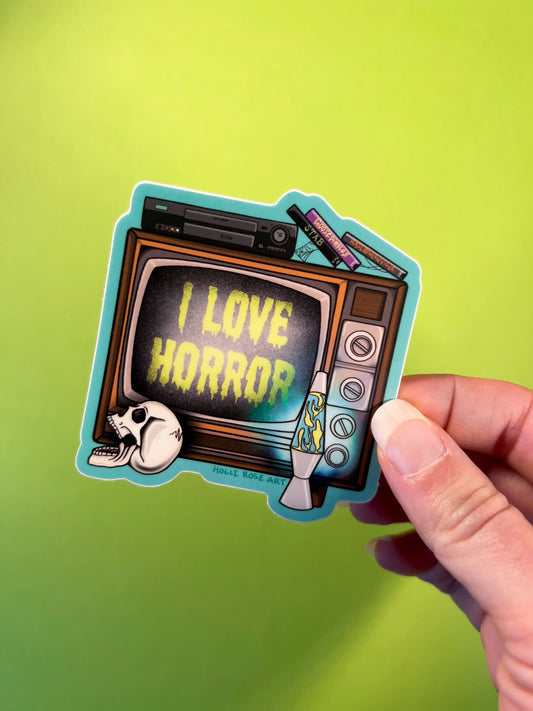 Sticker of a retro TV with 'I Love Horror' text held against a green background
