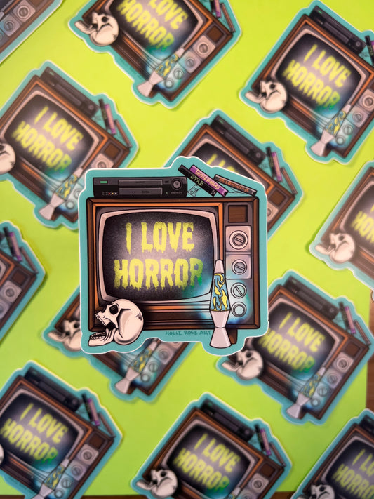Sticker of a retro TV with 'I Love Horror' text held against a green background