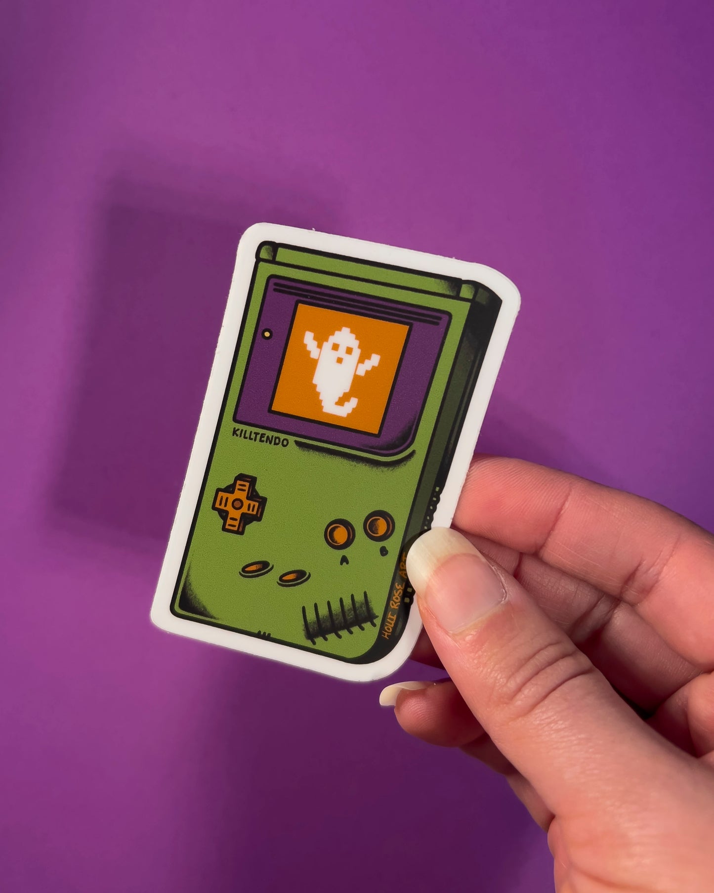 Sticker of a green hand gaming system with a ghost on the screen on a purple background