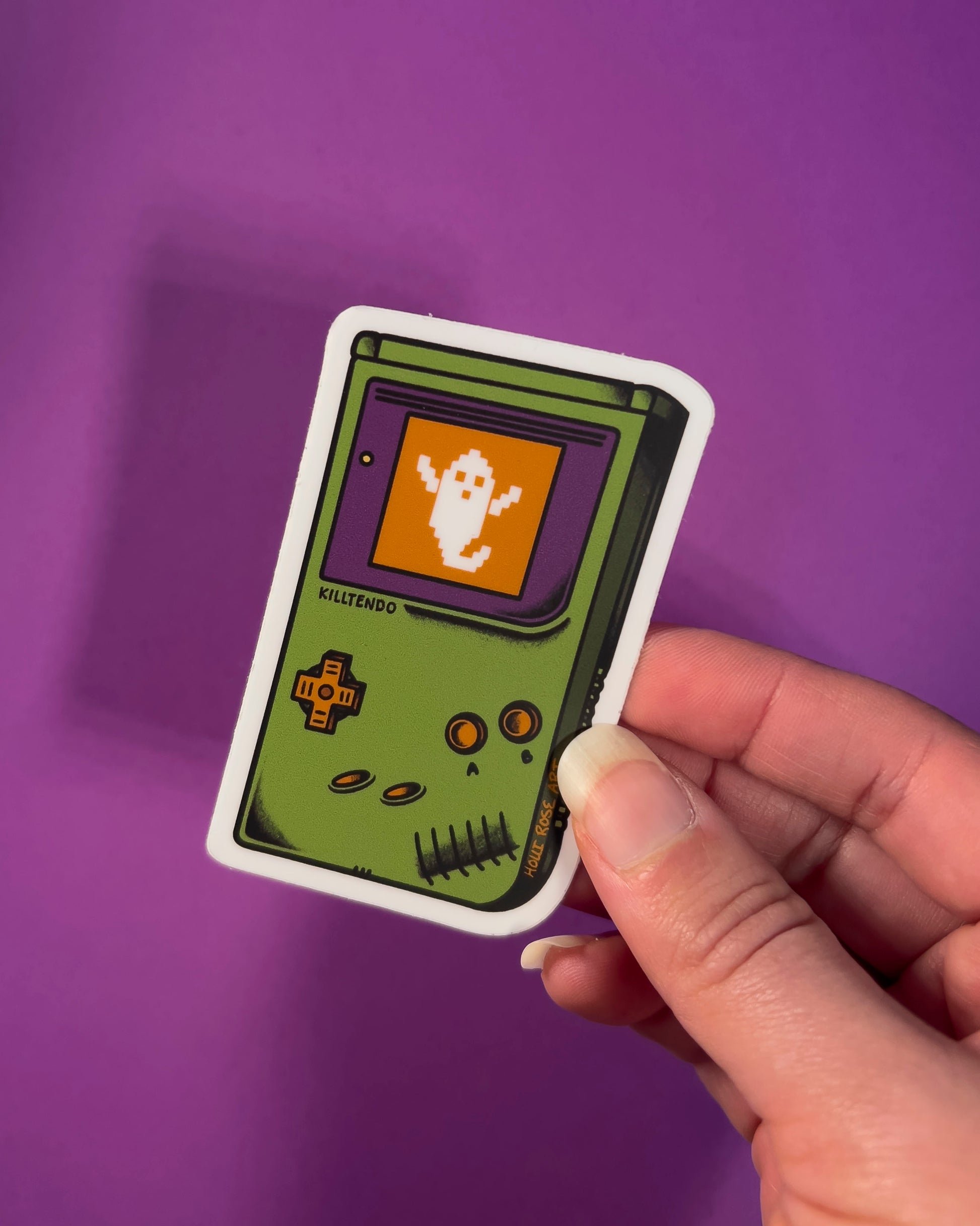 Sticker of a green hand gaming system with a ghost on the screen on a purple background