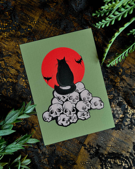 art print with a black cat  sitting on a pile of skulls