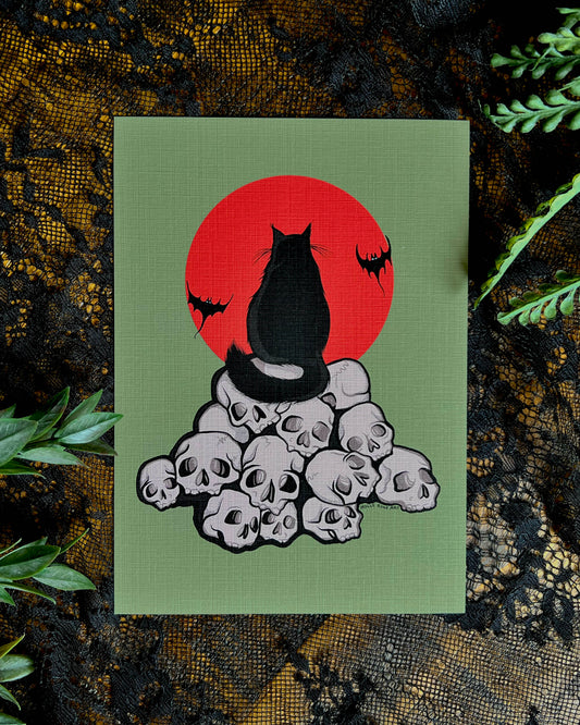 art print with a black cat  sitting on a pile of skulls