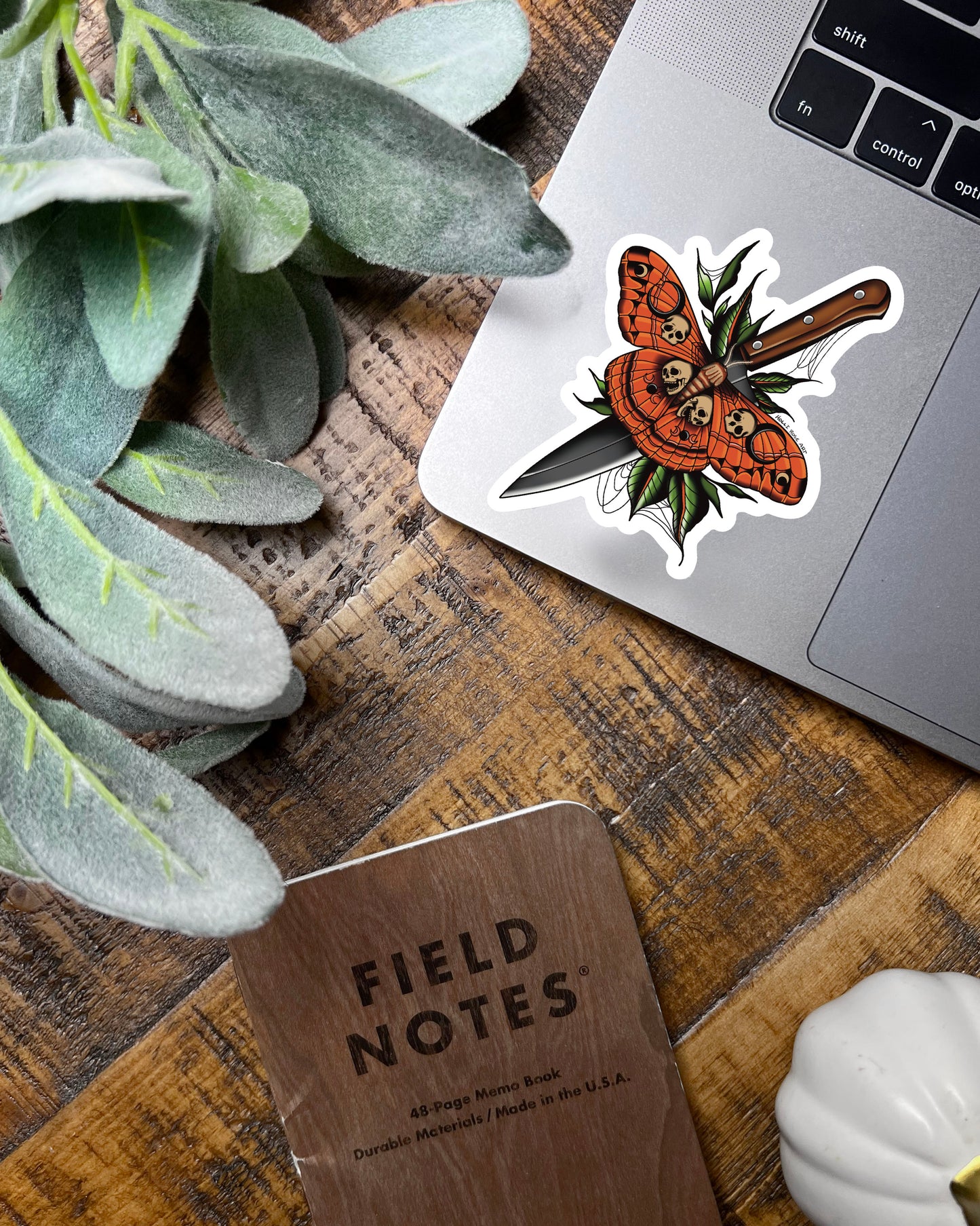 A sticker with a moth that as skulls on it and a knife behind it 