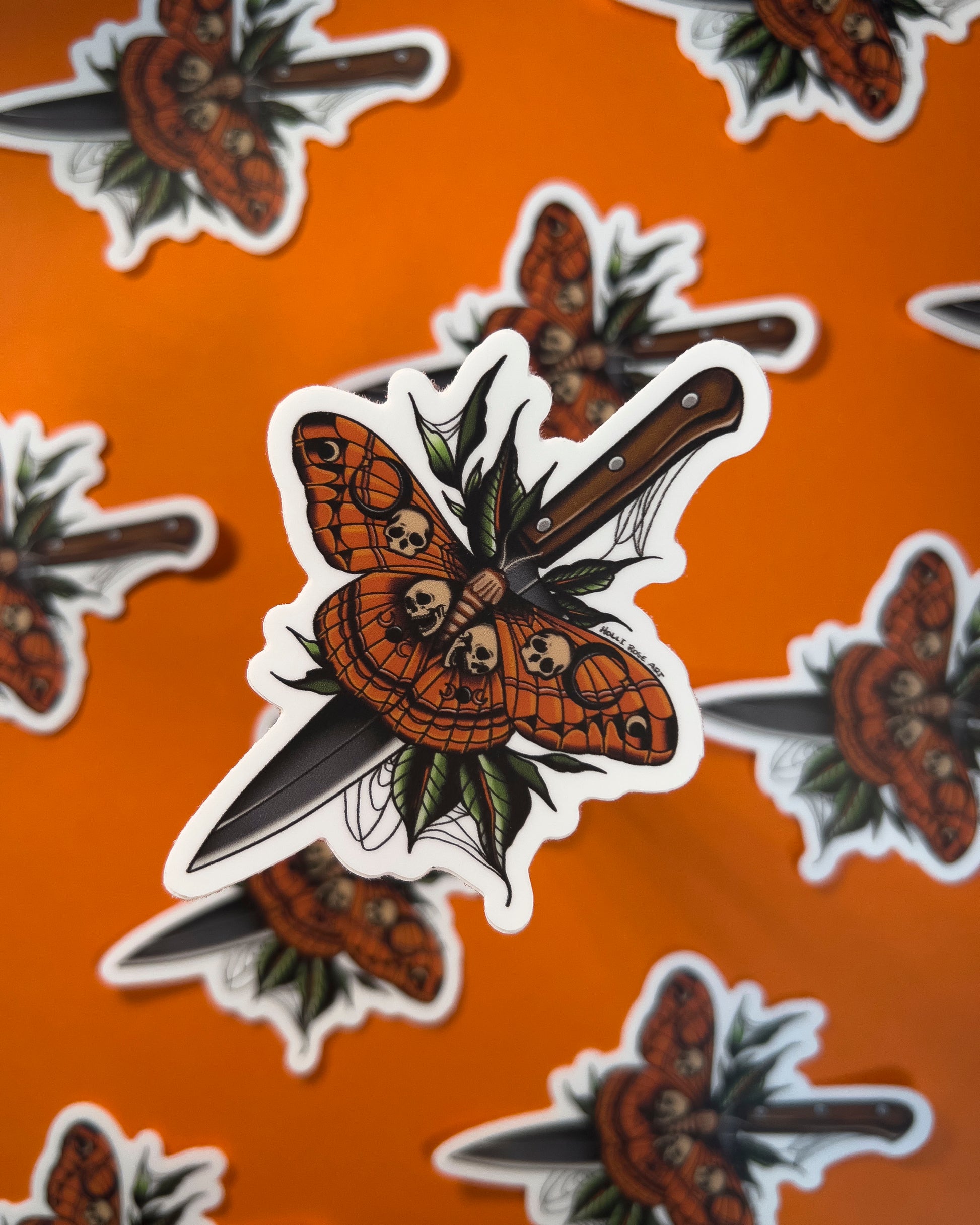 A sticker with a moth that as skulls on it and a knife behind it 