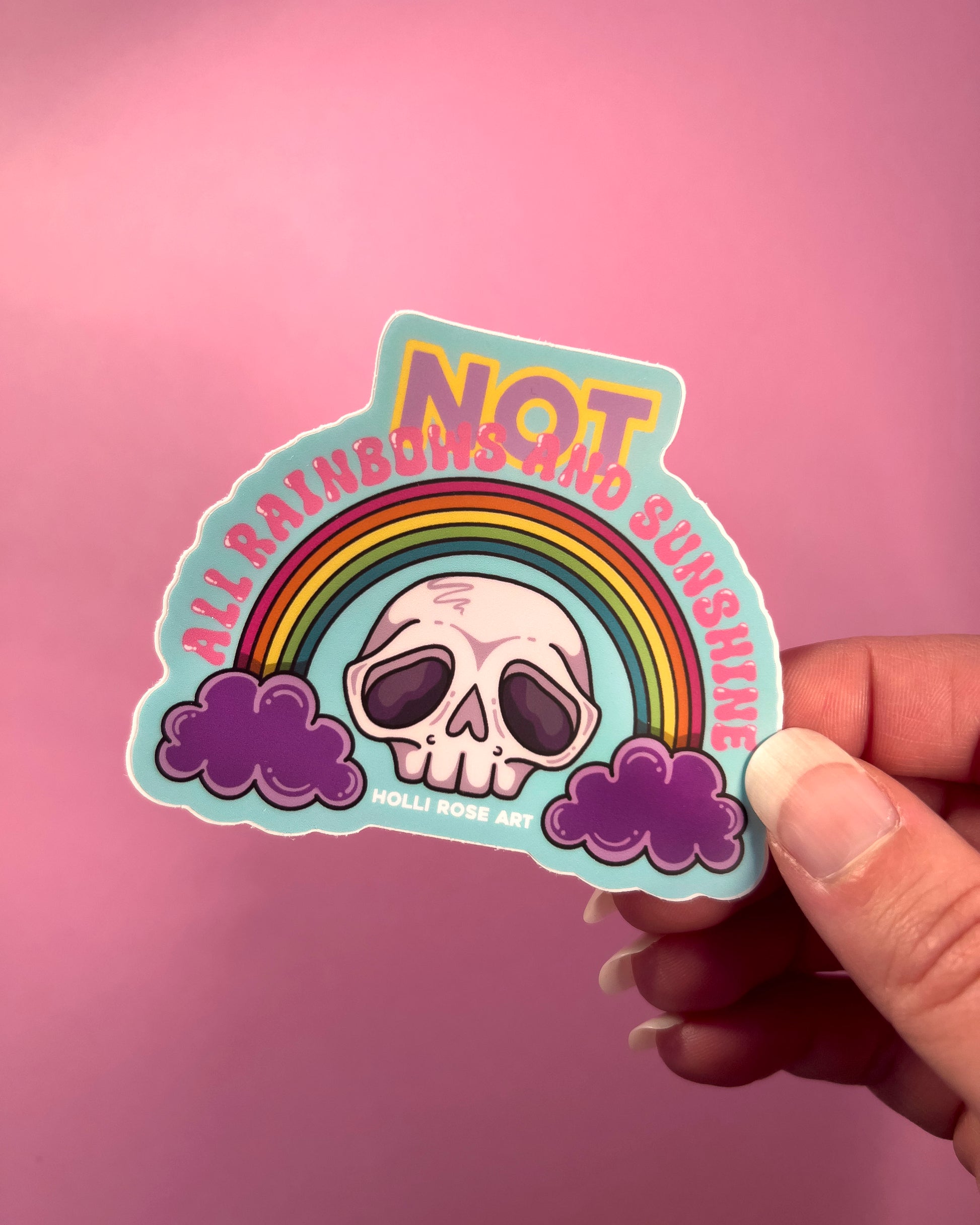 Sticker with skull and rainbow design on a pink background with flowers saying "Not all rainbows and sunshine"