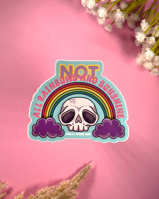 Sticker with skull and rainbow design on a pink background with flowers saying "Not all rainbows and sunshine"