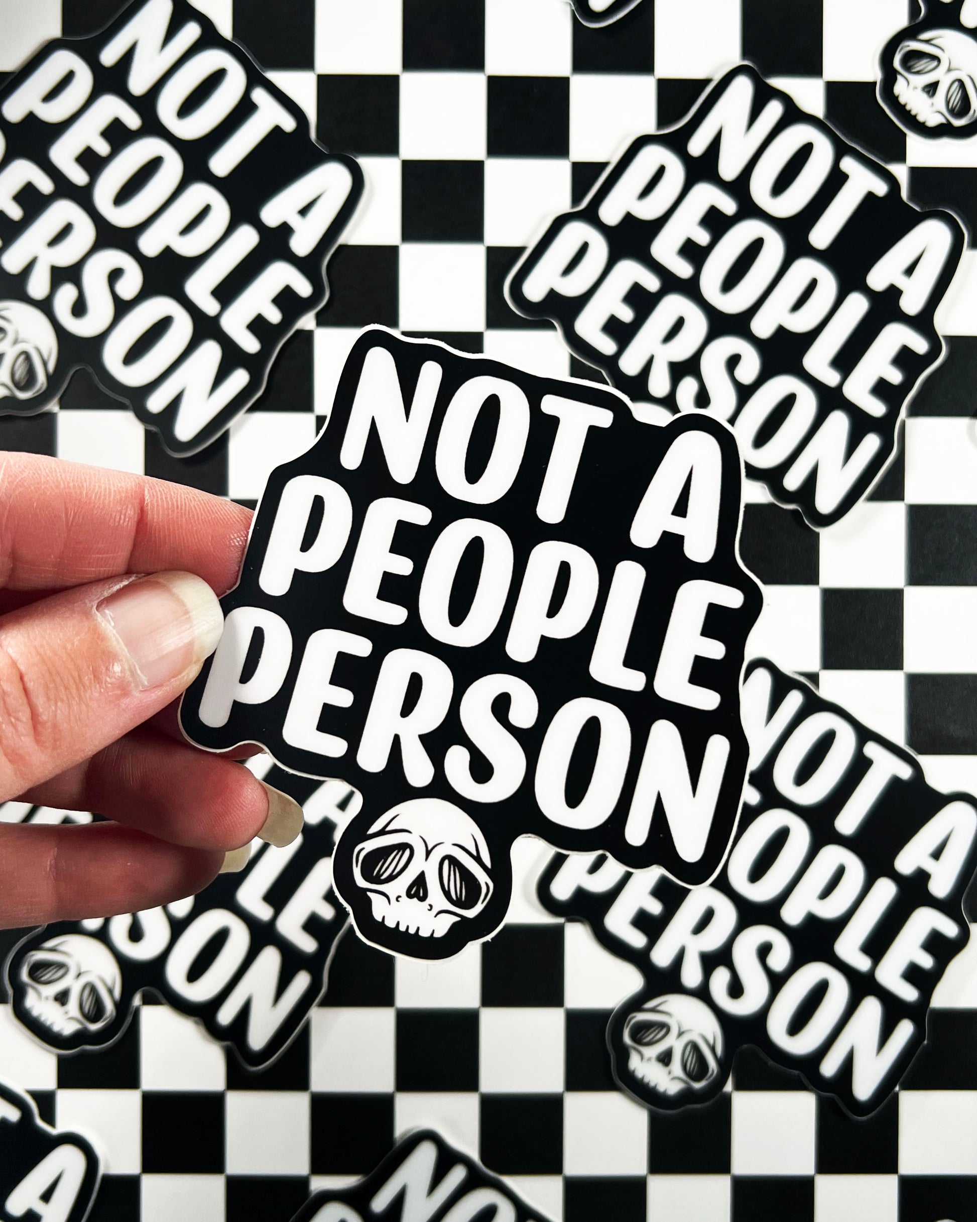 Sticker with 'Not a People Person' text held over a checkered background