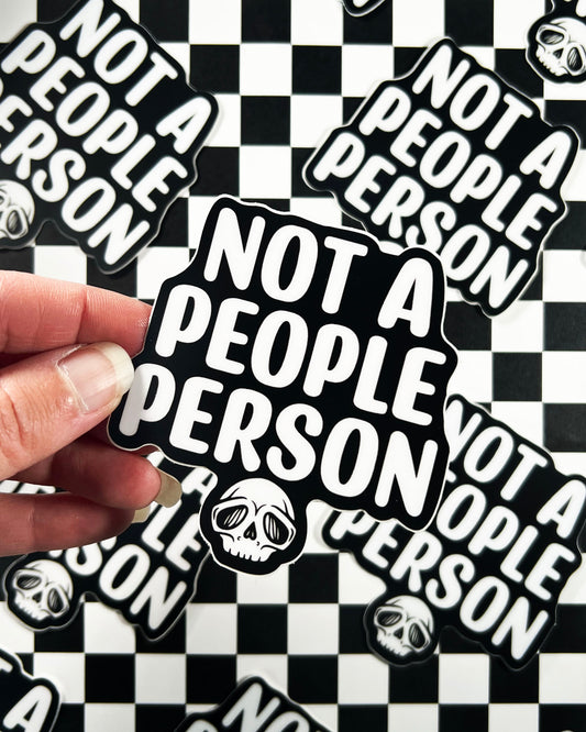 Sticker with 'Not a People Person' text held over a checkered background