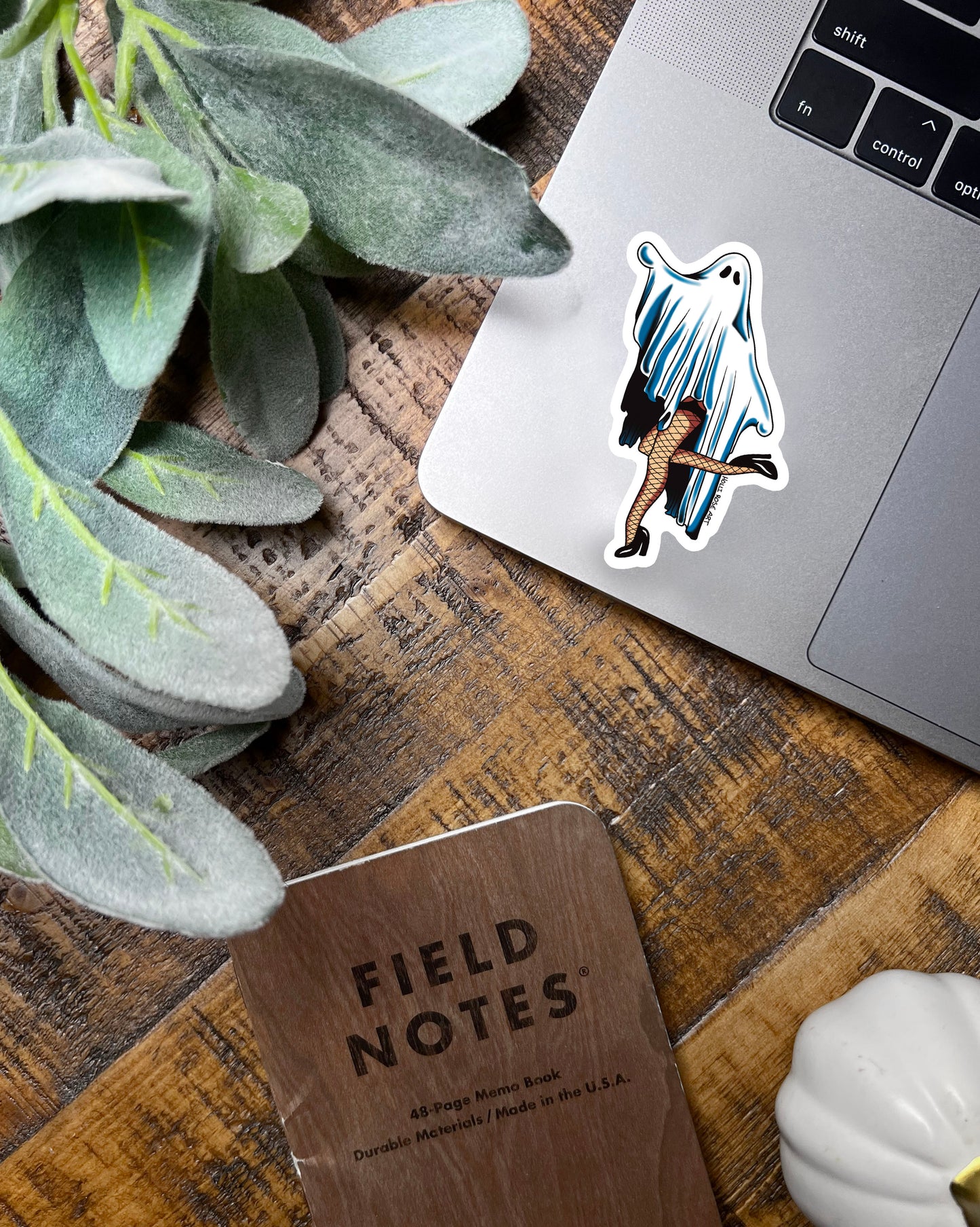 Sticker of a ghost in fishnet stockings on a teal background with flowers and leaves.