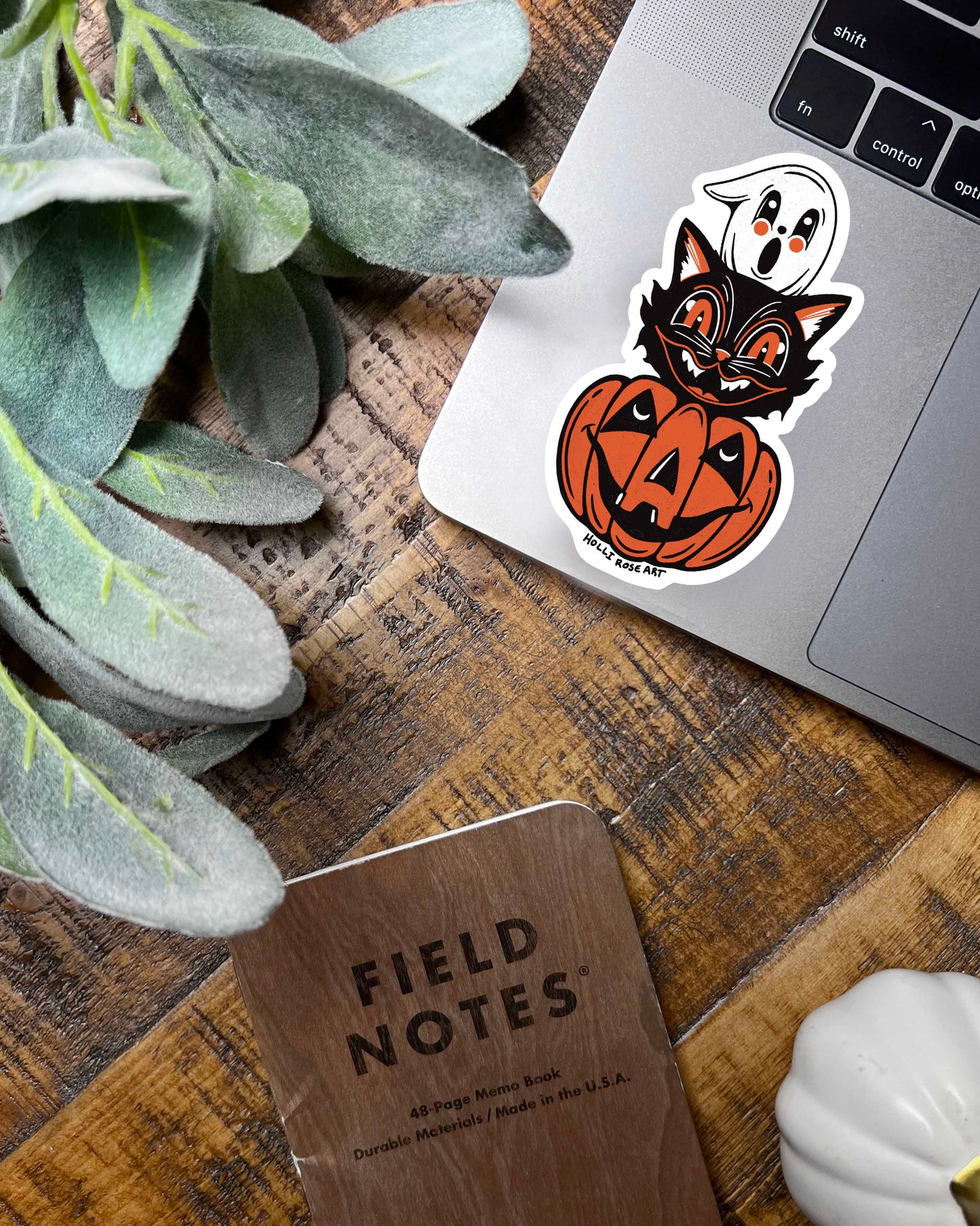 Halloween-themed sticker with a black cat, ghost, and pumpkin on a laptop