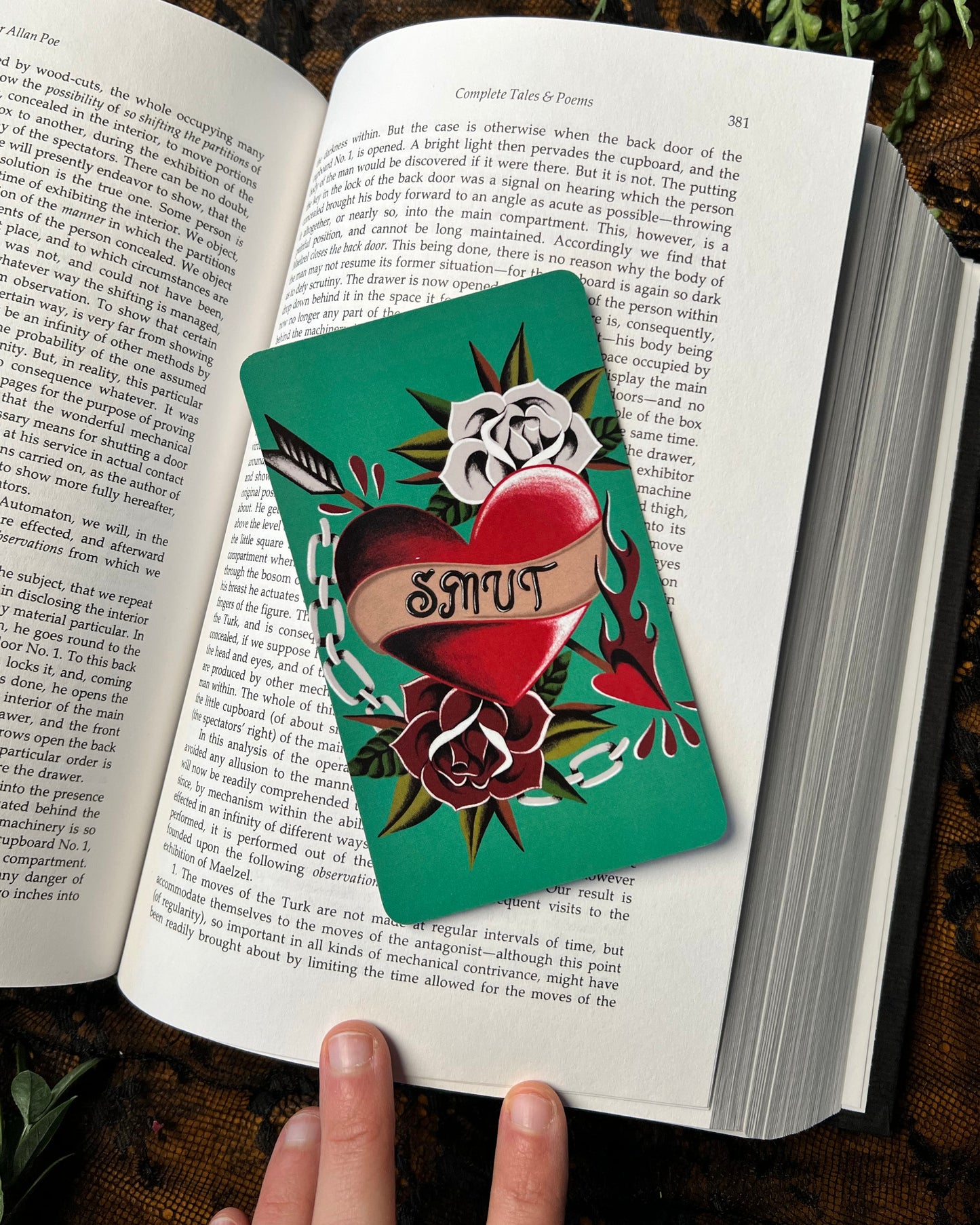 A colorful bookmark with a heart and floral design, featuring the word 'Smut', placed in an open book.
