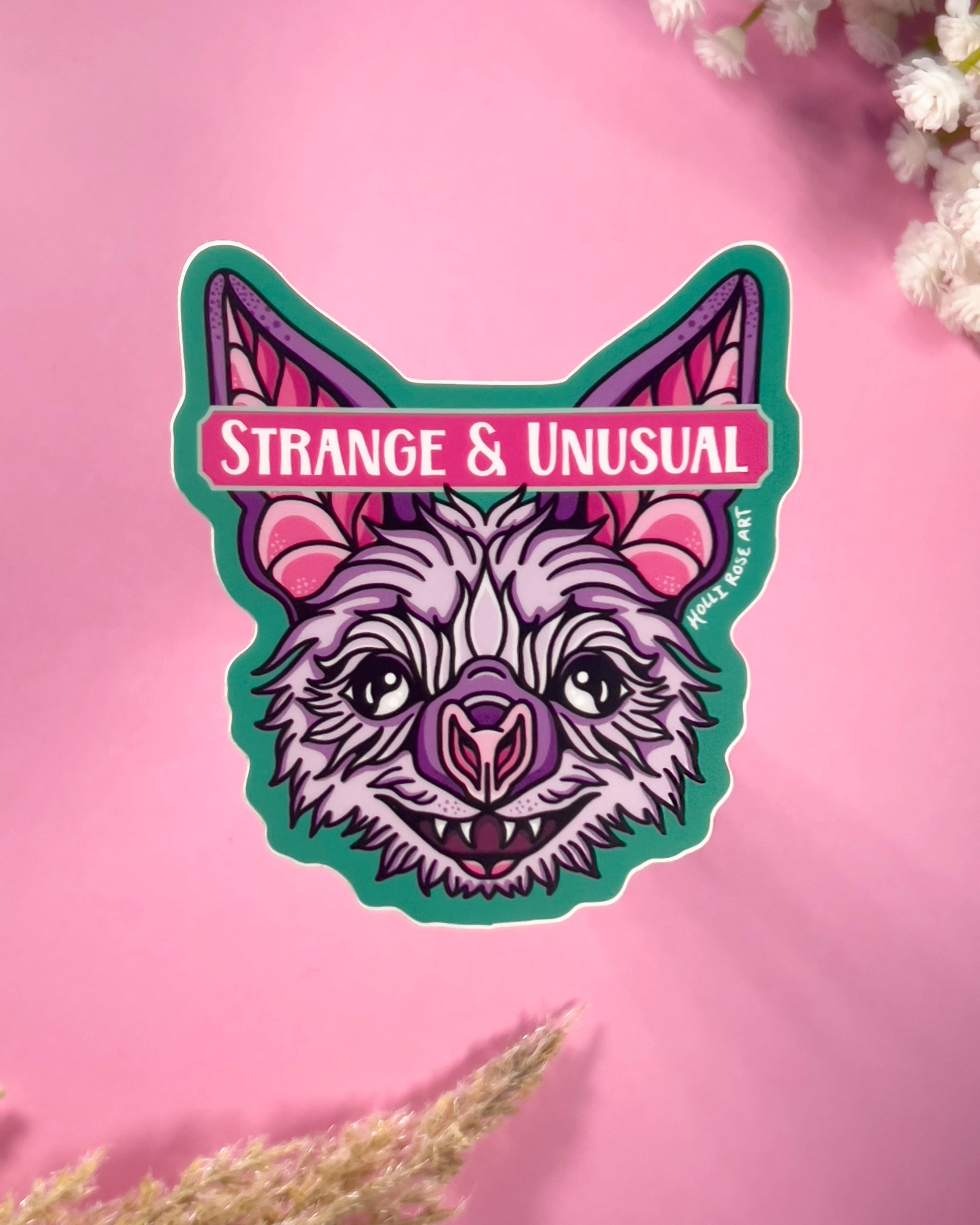 Sticker with a stylized bat design and 'Strange & Unusual' text on a pink background.