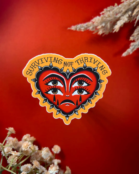 heart sticker with eyes that says "surviving not thriving"