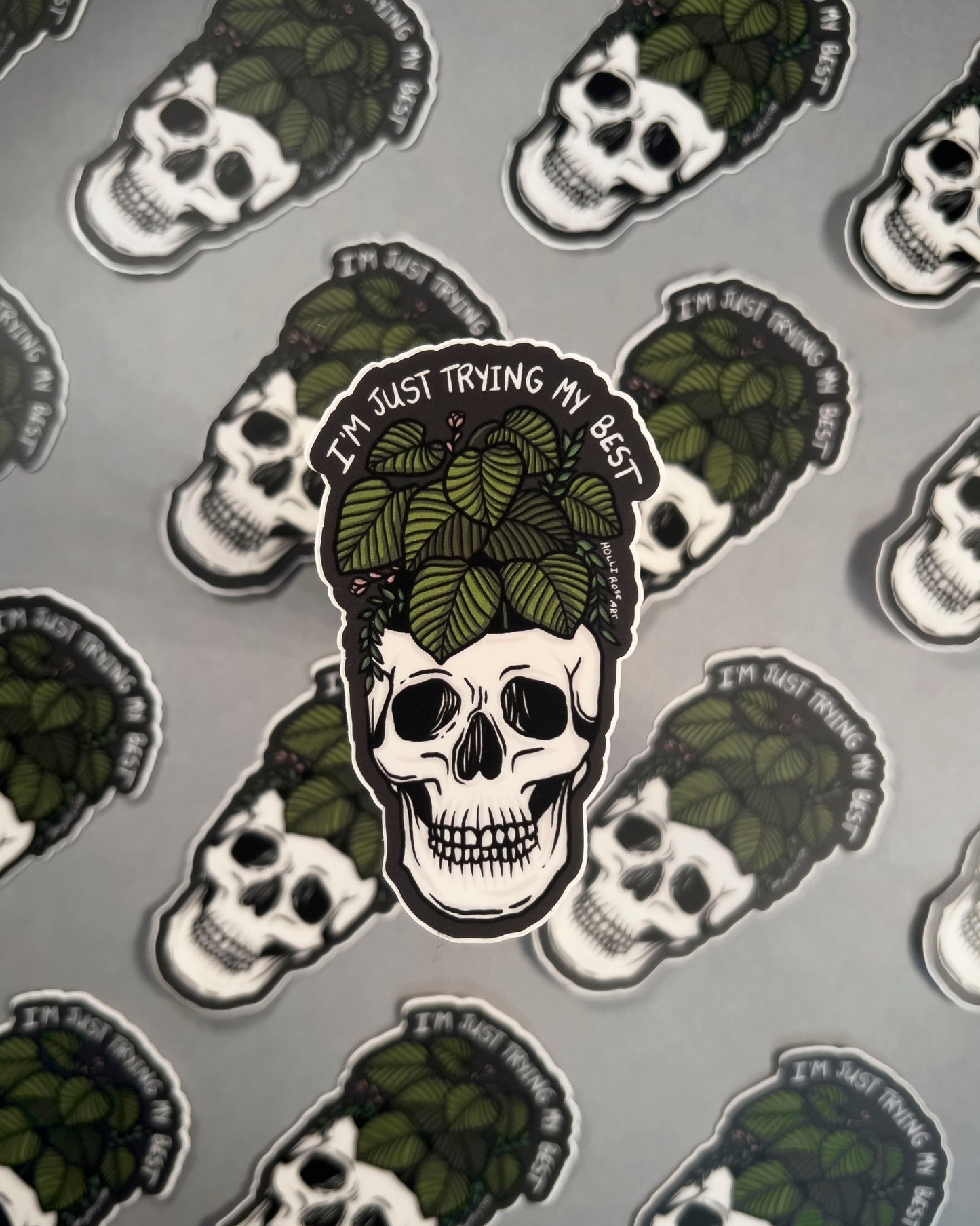 Skull with green leaves and text 'I'm just trying my best' on a gray background with similar skull designs.