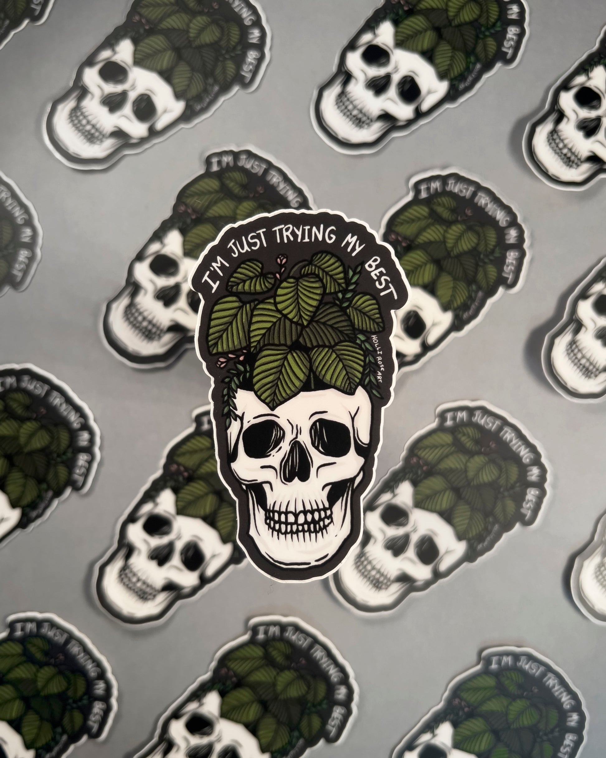 Skull with green leaves and text 'I'm just trying my best' on a gray background with similar skull designs.