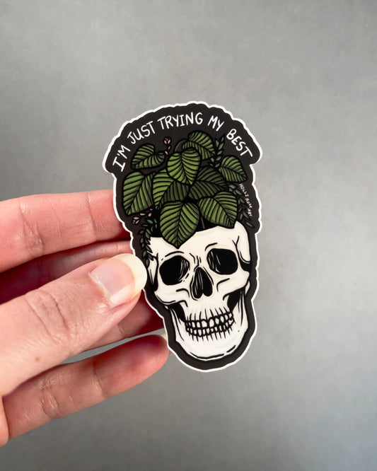 Skull sticker with leaves and text 'I'm just trying my best' on a gray background 