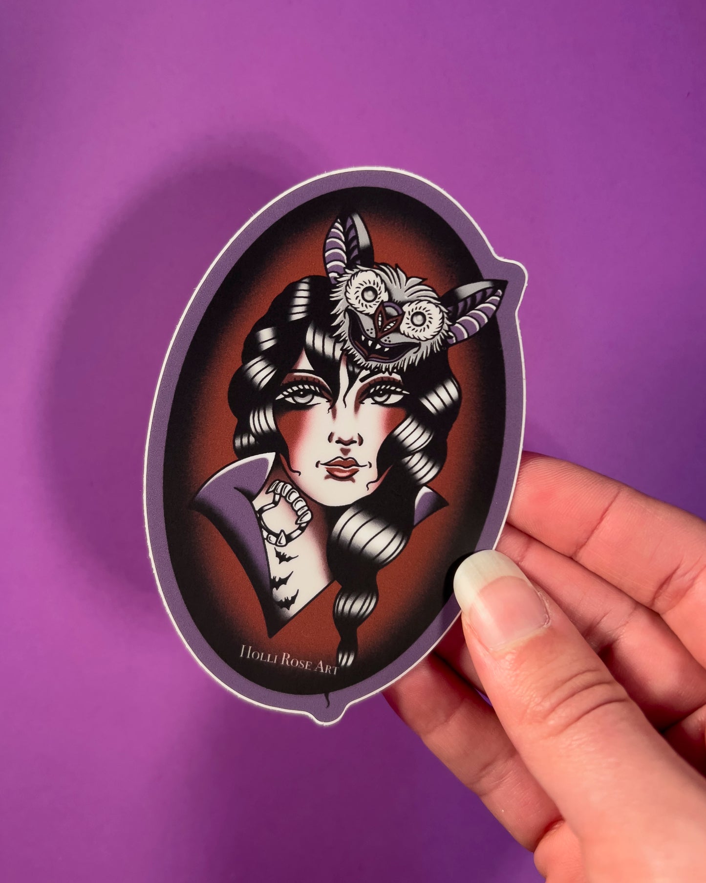 sticker with an American traditional vampire girl and a bat on her head in an oval shape and is purple and red