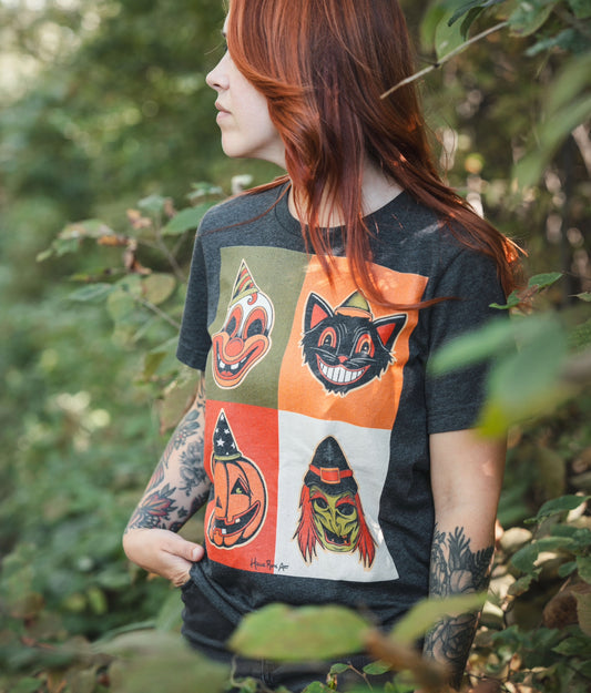Holli Rose Art Wearing A dark grey t-shirt featuring a square arrangement of four different classic Halloween mask designs, including a pumpkin, a clown, a witch, and a cat