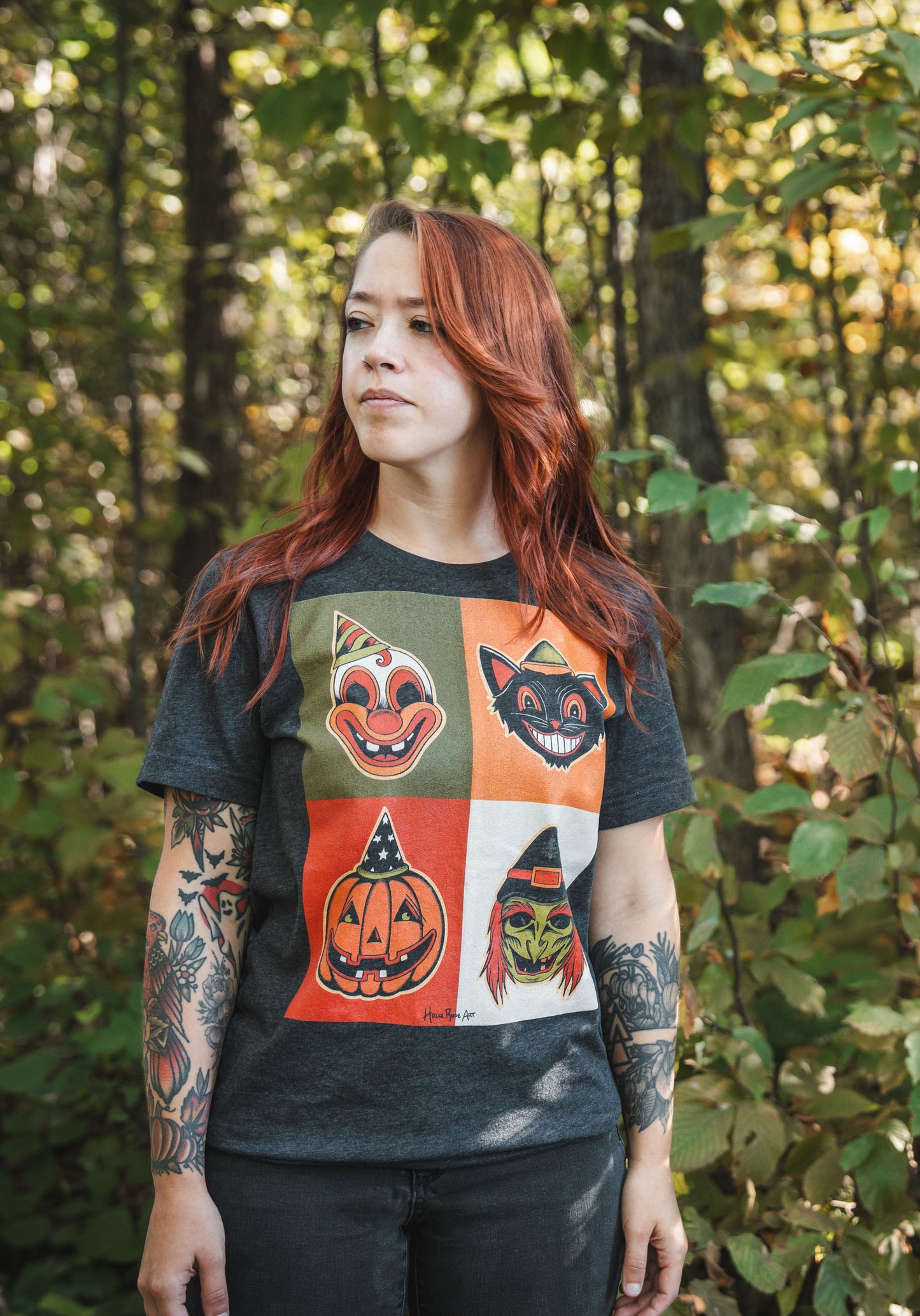 Holli Rose Art wearing A dark grey t-shirt featuring a square arrangement of four different classic Halloween mask designs, including a pumpkin, a clown, a witch, and a cat